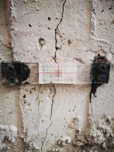 Close-Up Of A Concrete Wall With A Vertical Crack And A Measurement Gauge Attached, Showing Foundation Damage Being As