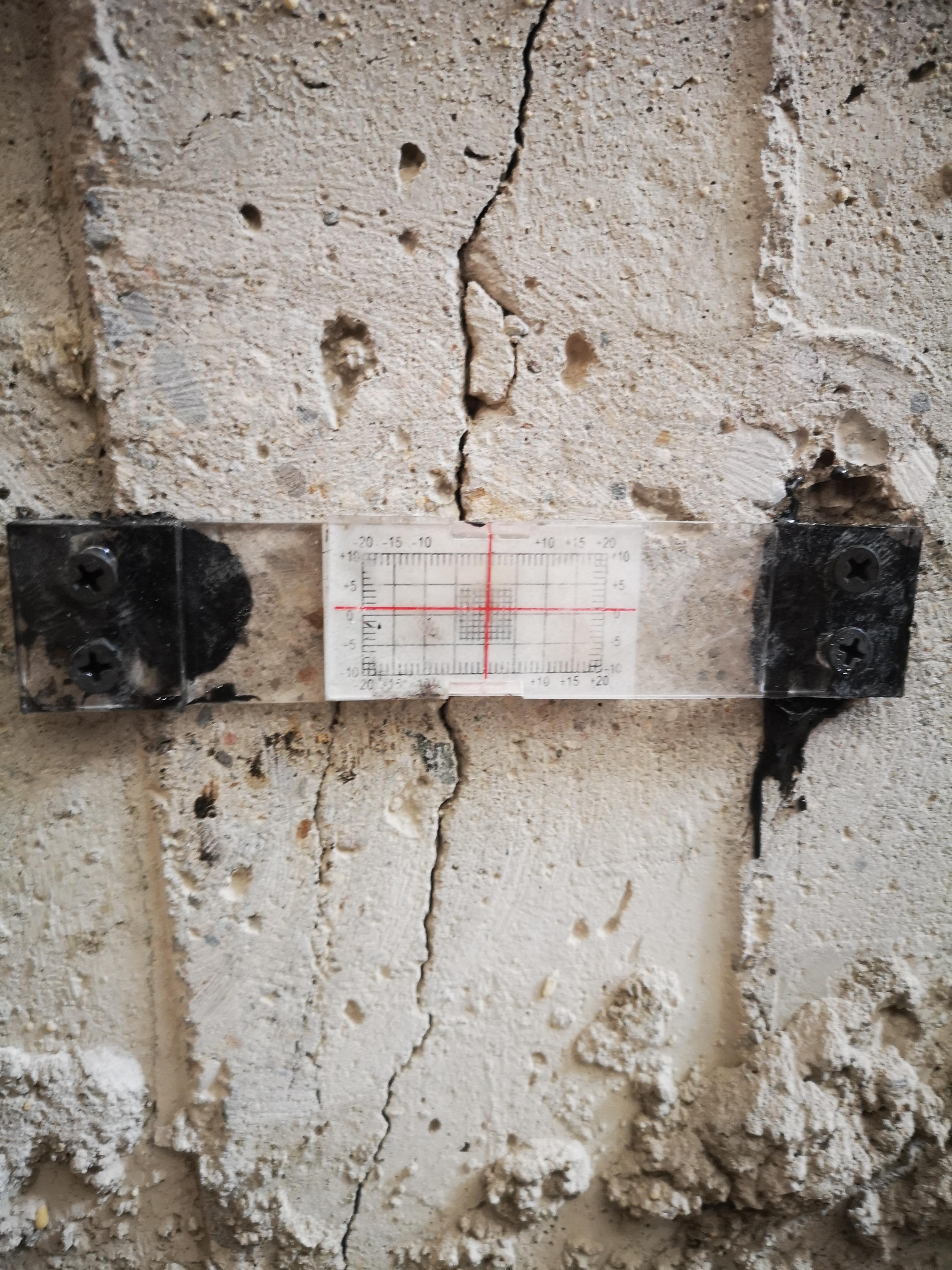 Close-Up Of A Concrete Wall With A Vertical Crack And A Measurement Gauge Attached, Showing Foundation Damage Being As
