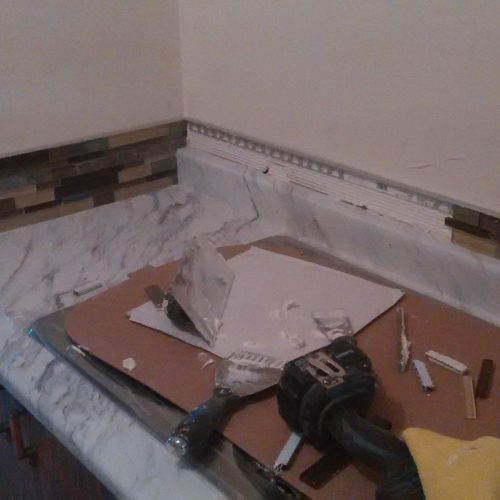 Corner Of A Kitchen Countertop With Marble-Patterned Surface And Decorative Tile Backsplash In Progress, Showing Tools