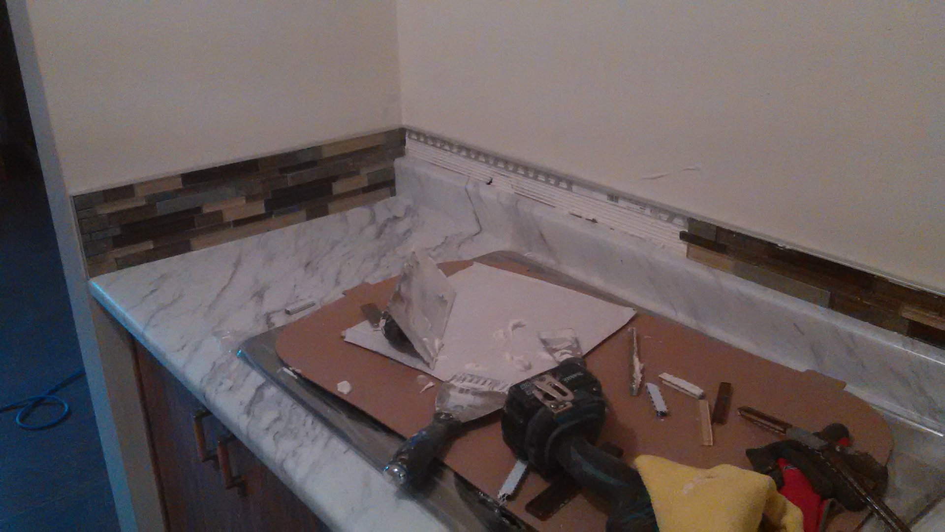 Corner Of A Kitchen Countertop With Marble-Patterned Surface And Decorative Tile Backsplash In Progress, Showing Tools
